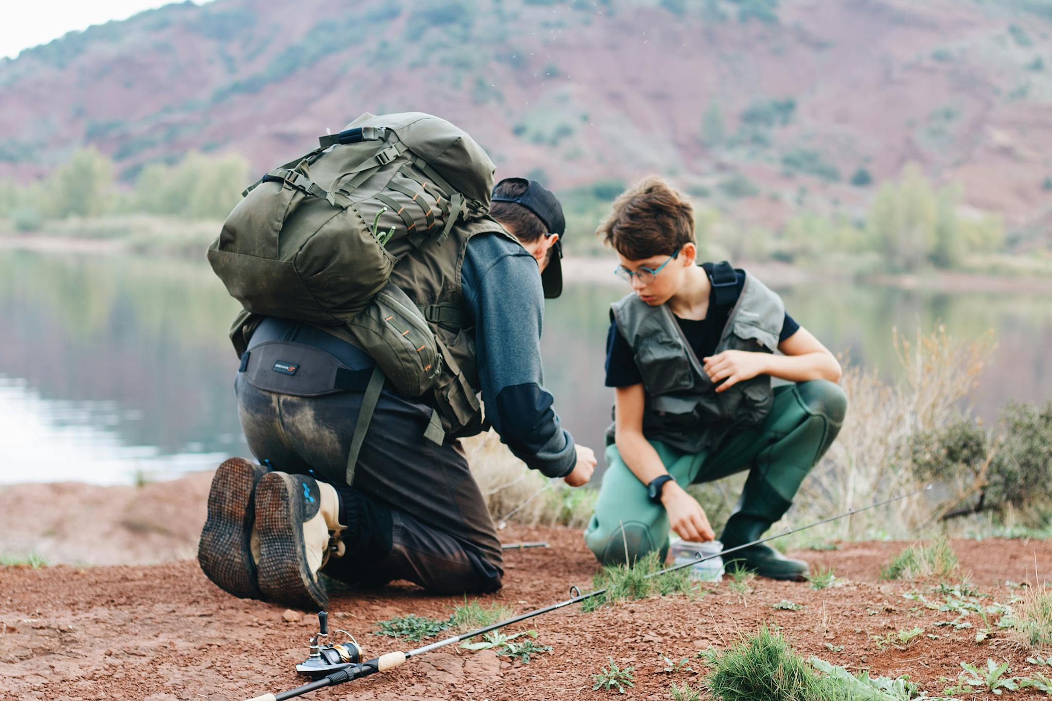 Father and son bonding over a fishing trip by a serene lake in an outdoor setting.