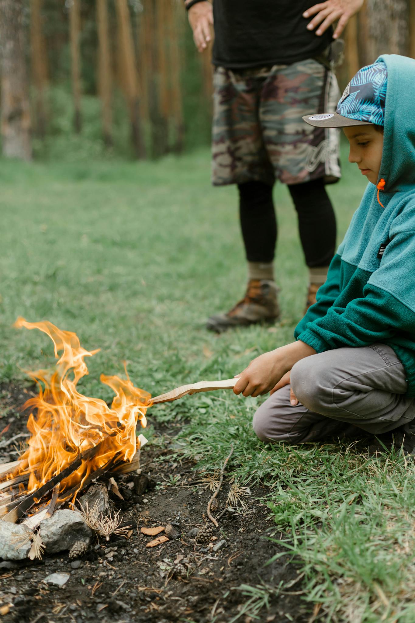 Young boy learning to manage a campfire with adult supervision in Russian outdoors.